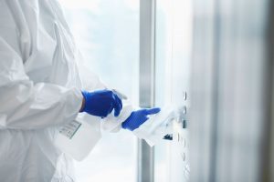 A person wearing gloves and a white suit spraying a solution on a wipe.