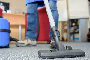 A person using a vacuum to clean a carpet.