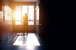 A person mopping the floor of a commercial building. The sun is setting in the background through the window.